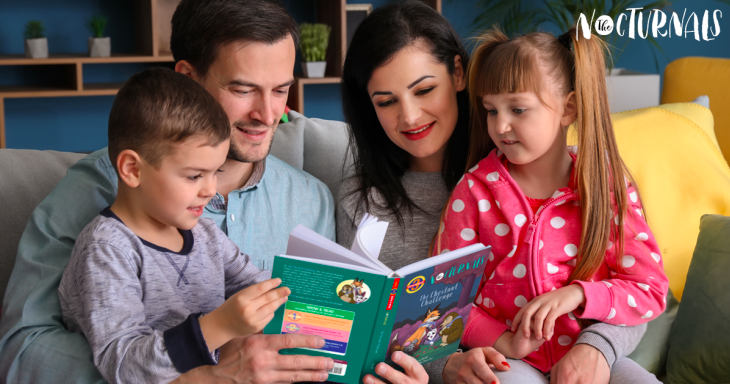 A boy, who is sitting on his fatherâ€™s lap, is turning the pages of The Nocturnals: The Chestnut Challenge. Next to them on the couch is the mother who is carrying a pigtailed girl on her lap. 