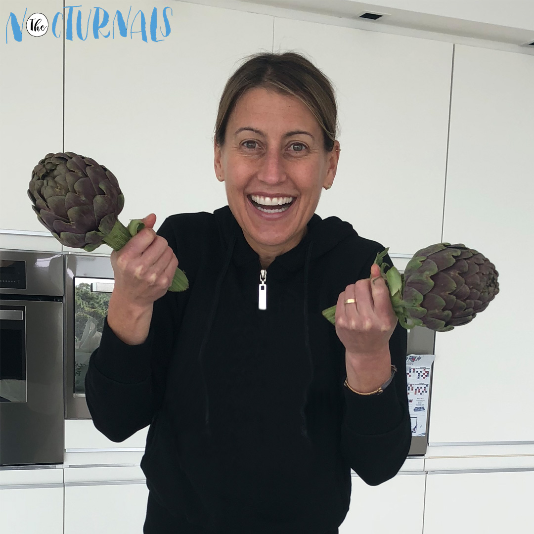 Tracey Hecht, the author of The Nocturnals, is holding up two heads of artichokes in her kitchen.   