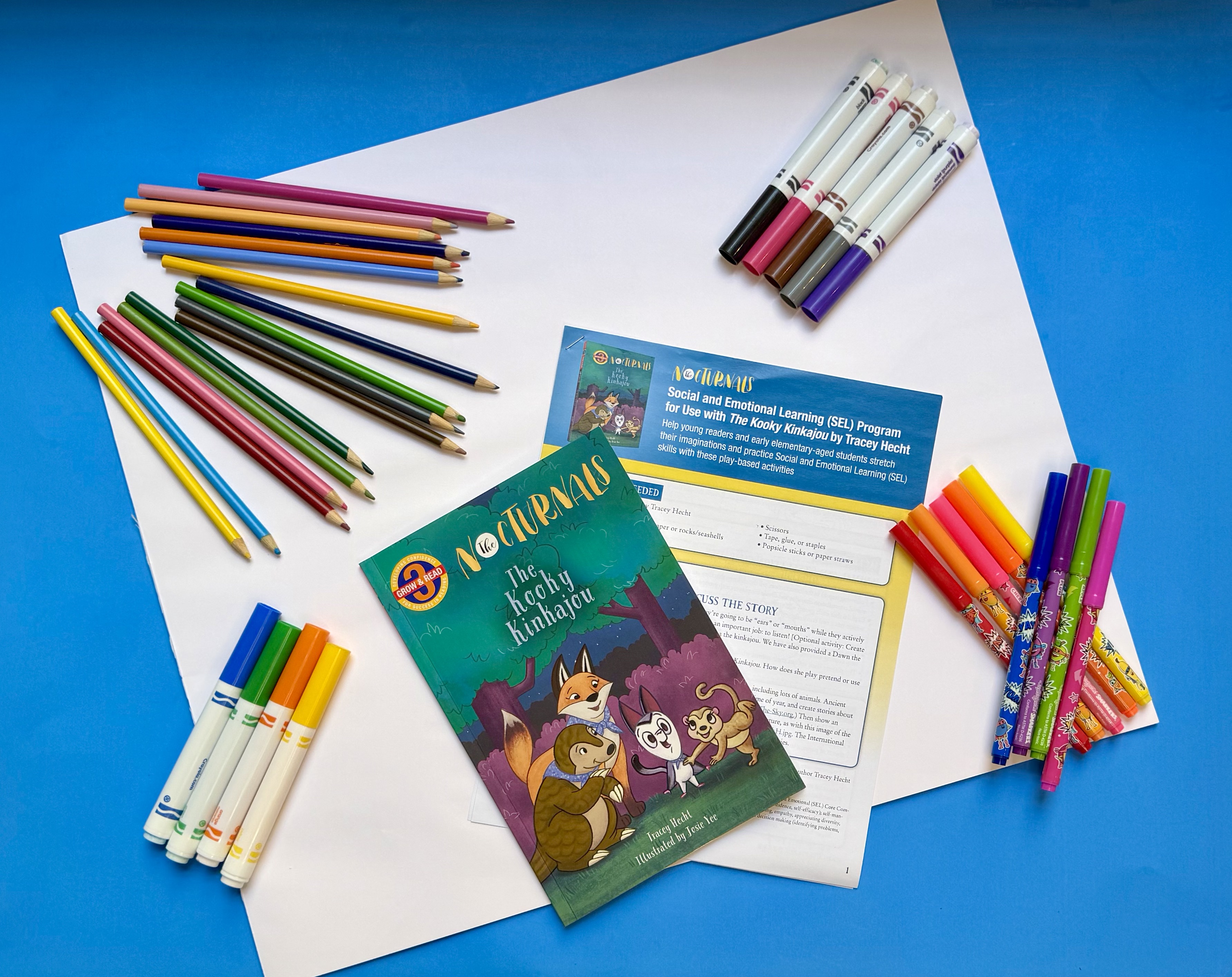 The image shows the Kooky Kinkajou book, markers, pencils, and paper.