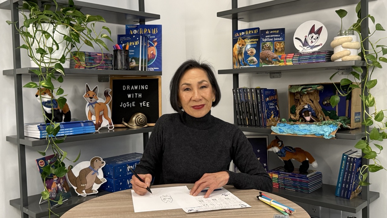 Illustrator Josie Yee sitting at a table drawing Bismark the sugar glider from The Nocturnals