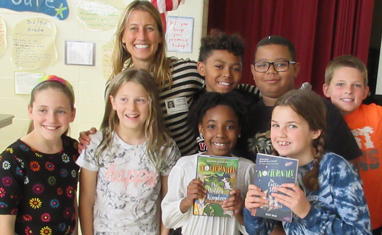 Tracey Hecht, the author of the Nocturnals, is posing with a group of middle grade students. Two girls at the front of the picture are holding up copies of The Nocturnals: Hidden Kingdom and The Nocturnals: The Fallen Star. 